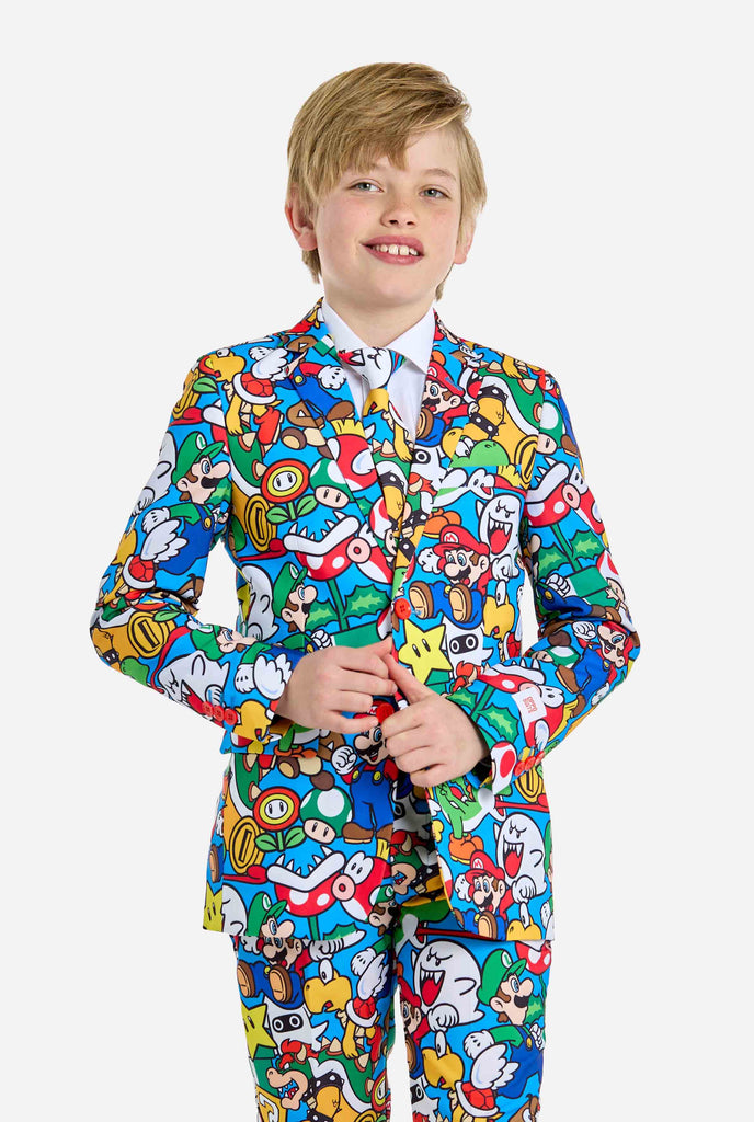 Image of teen wearing a Super Mario all-over print suit, consisting of blazer, pants and tie. Main color is blue, but there is also yellow, red and white.