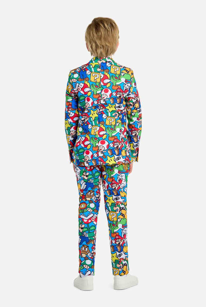 Image of teen wearing a Super Mario all-over print suit, consisting of blazer, pants and tie. Main color is blue, but there is also yellow, red and white. View from the back.