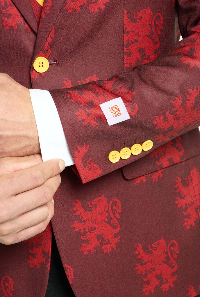 Image with light grey background and man wearing Harry Potter suit, Gryffindor styled. Suit consists of red blazer with Gryffindor logo and light red lions all over print, black pants, and red and yellow diagonal striped tie. Sleeve close up.   