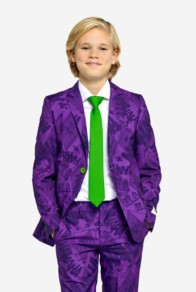 Teen wearing purple teen boys suit with a The Joker theme. Further he is wearing a green tie and a with shirt. Hands in pockets of pants.