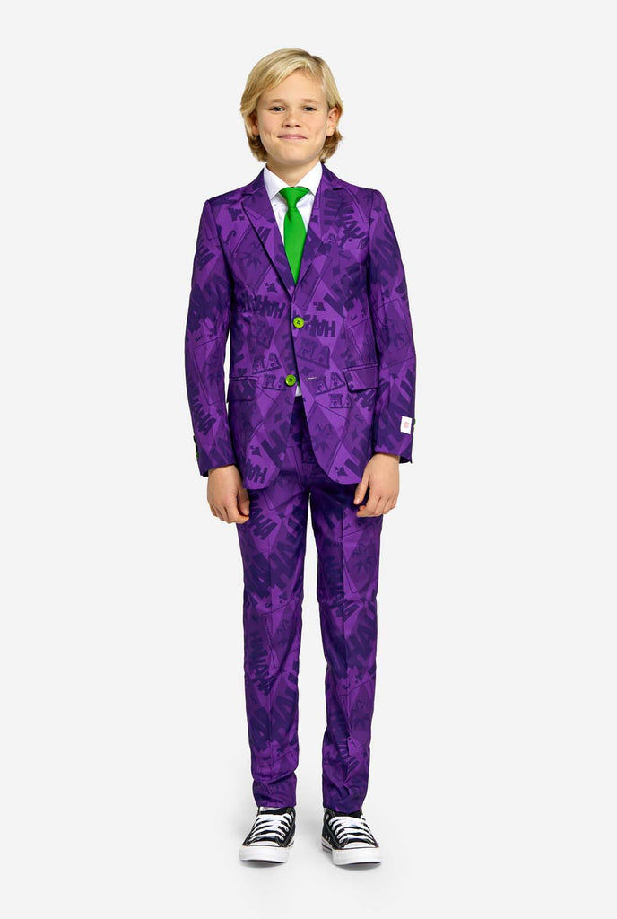 Teen wearing purple teen boys suit with a The Joker theme. Further he is wearing a green tie, a with shirt and black and white sneakers.