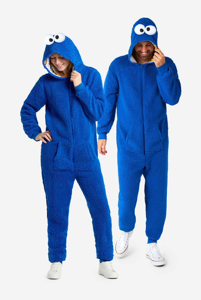 Man and Woman wearing blue pluche Cookie Monster Adult onesie for adults. Standing next to each other, holding hood with one hand.