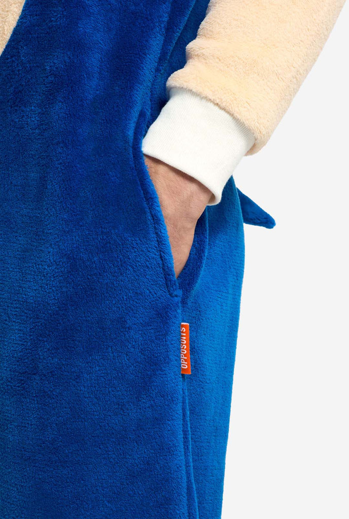 A person is dressed in a cozy, blue Sonic the Hedgehog adult onesie, featuring soft beige sleeves to replicate Sonic's iconic look. This Sonic the Hedgehog onesie is ideal for cosplay, lounging, or themed events. Close up from side pocket with hand in pocket.