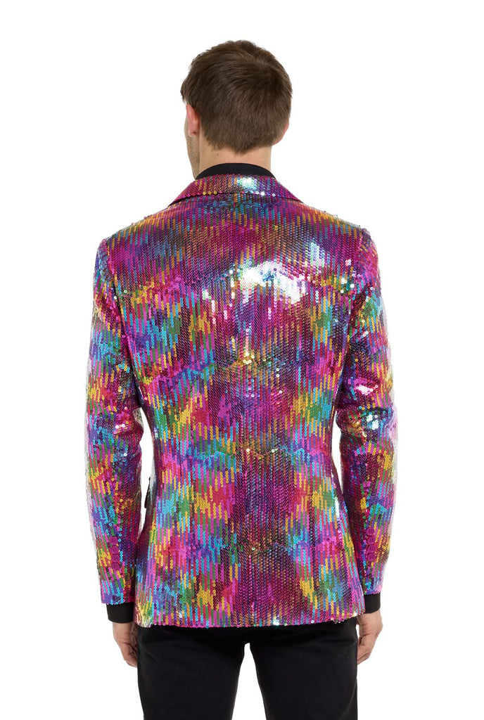 Image with white background and man wearing rainbow colored sequins blazer. Man also wearing black shirt and black pants. Man facing away from the camera and showing his back. 