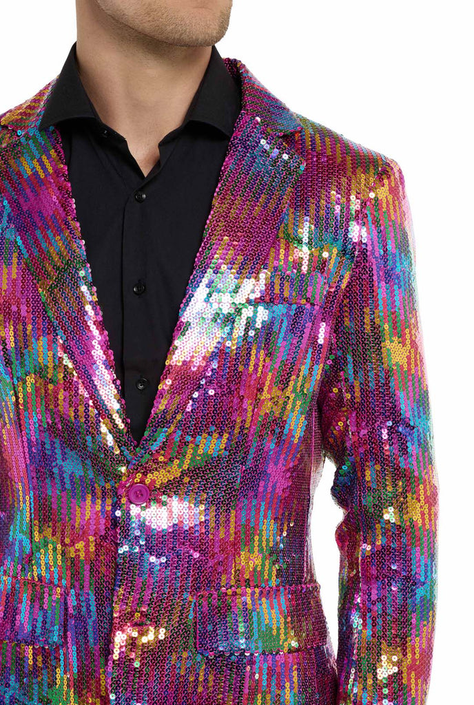 Image with white background and man wearing rainbow colored sequins blazer. Man also wearing black shirt and black pants. Chest close up.