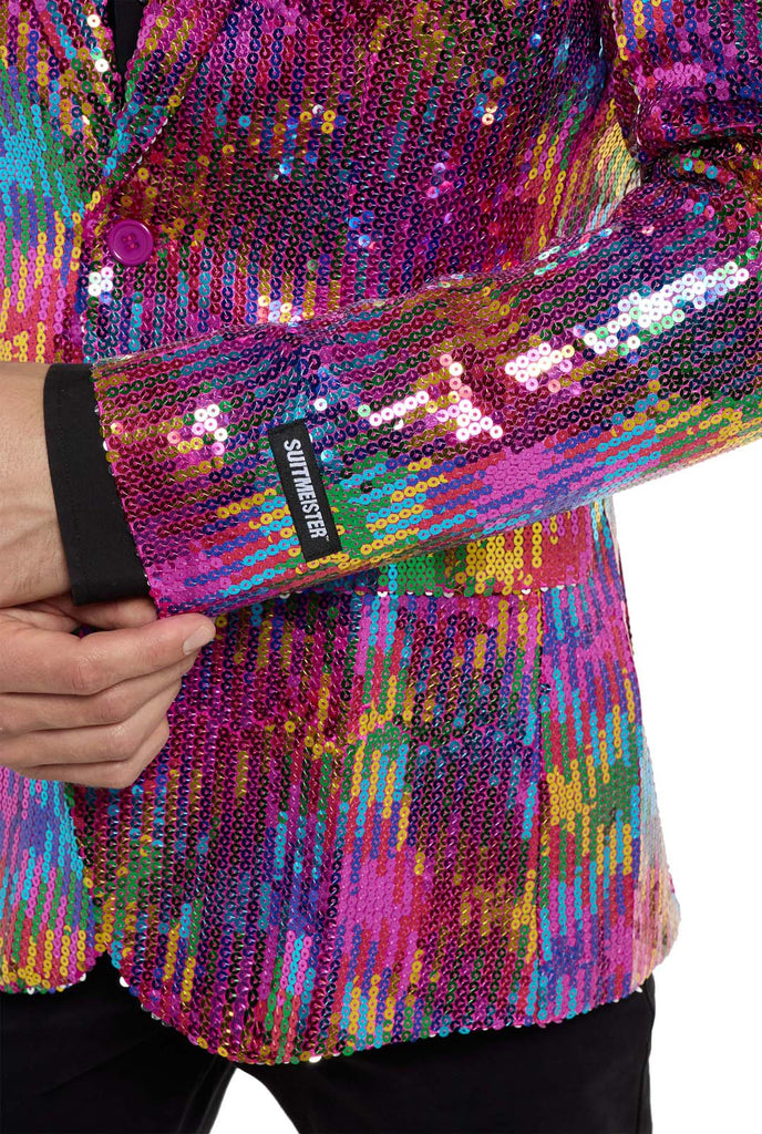 Image with white background and man wearing rainbow colored sequins blazer. Man also wearing black shirt and black pants. Sleeve close up.