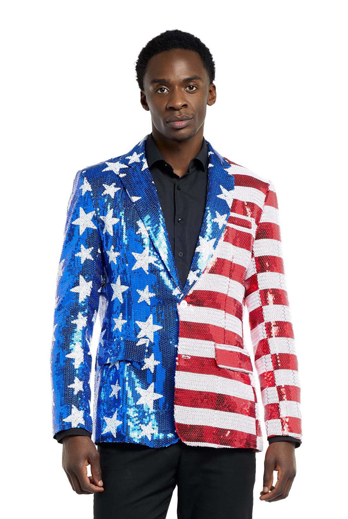 Image with white background and man wearing USA flag-colored red, blue and white sequins blazer. The man is also wearing black shirt and black pants.