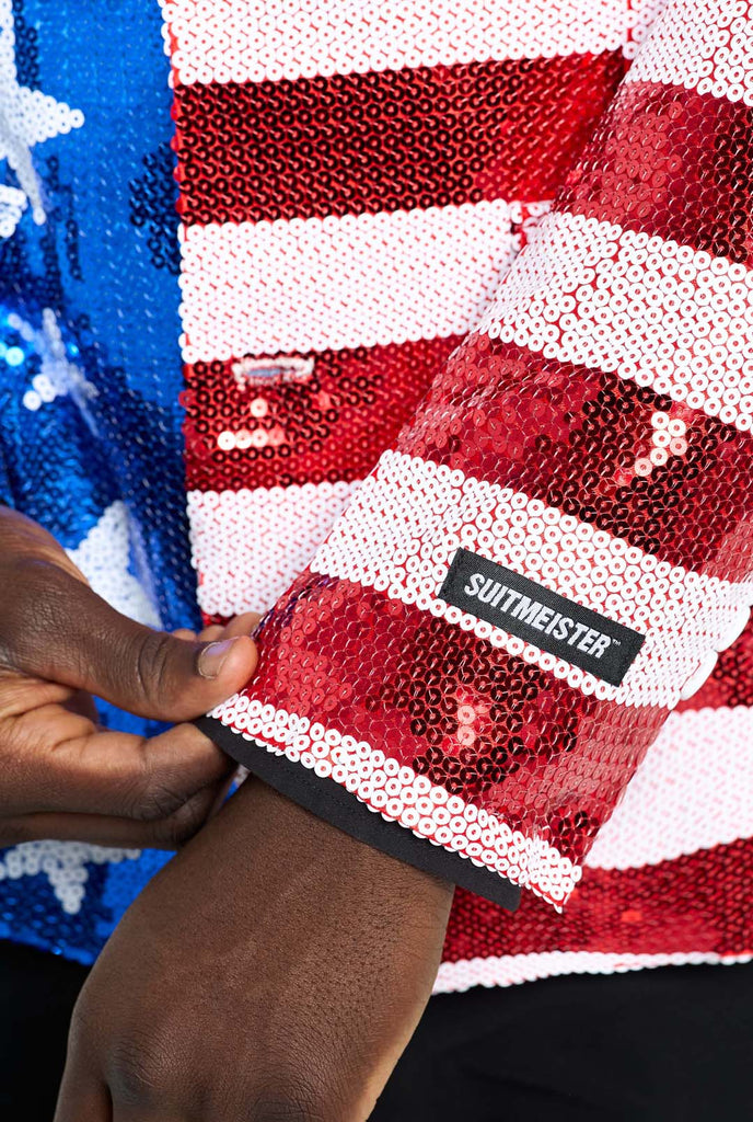 Image with white background and man wearing USA flag-colored red, blue and white sequins blazer. The man is also wearing black shirt and black pants. Sleeve close up.