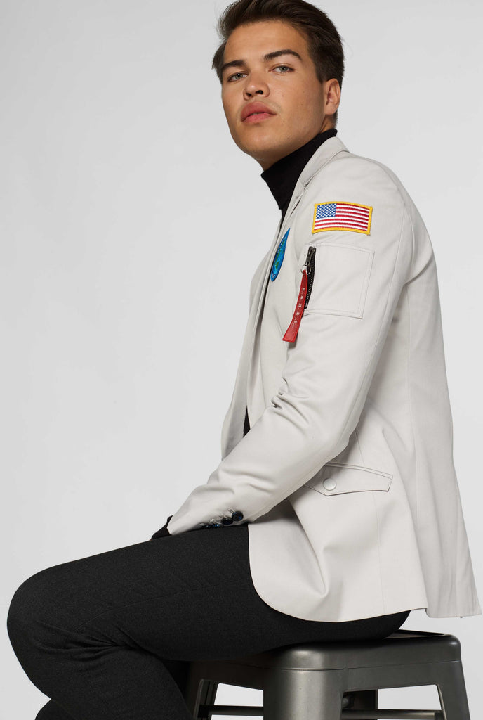 Light grey blazer with astronaut themed patches worn by man sitting down shown from the side