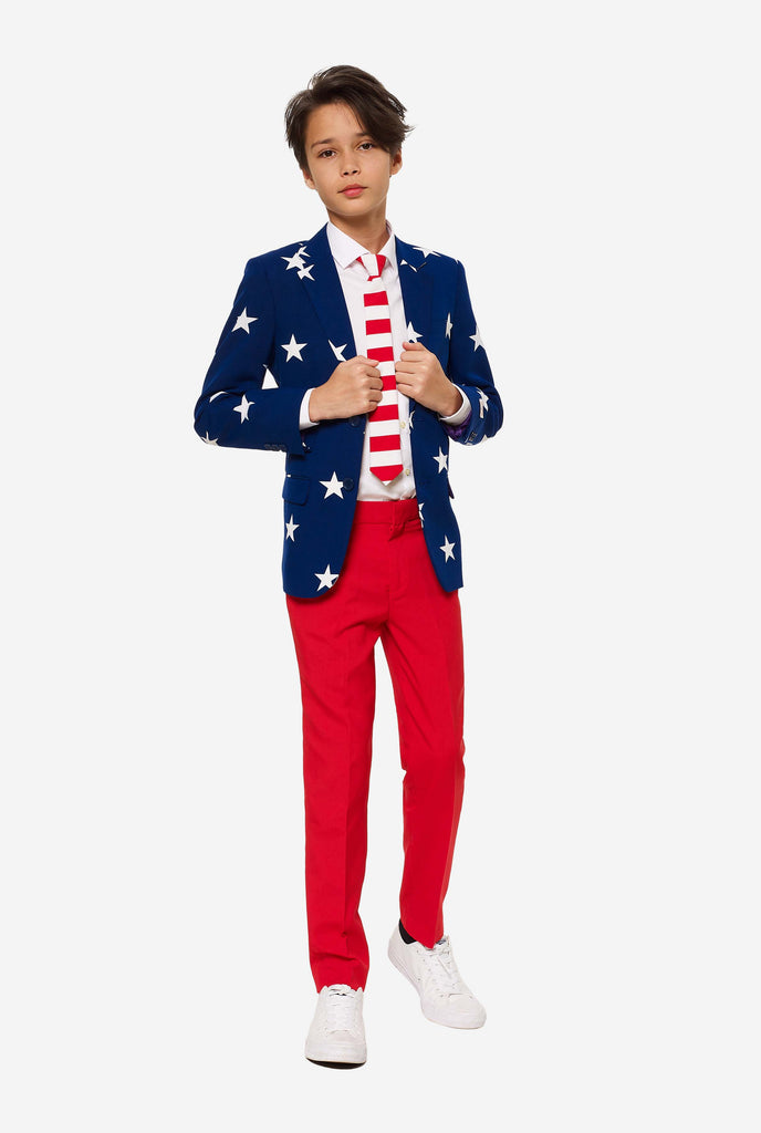 Teen wearing formal USA themed fourth of July suit, consisting of blue jacket and red pants. 